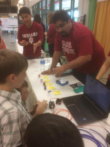 Ye group member describing a set of scientific items to a group of children